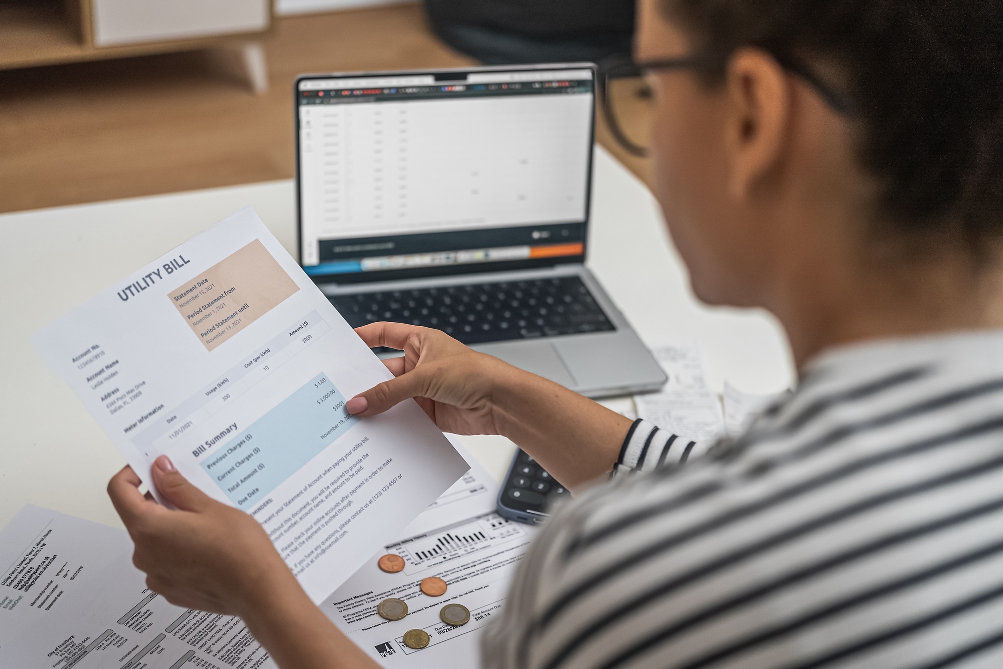 Concentrated woman examines documents with utilities for payment sitting at table with laptop