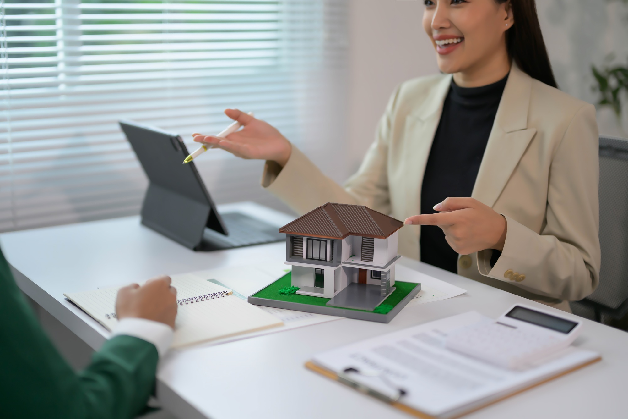 Real Estate Agent Discussing Property with Client Using Model House and Documents in Modern Office