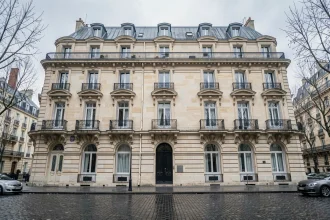 Façade haussmannienne typique à Paris avec balcons en fer forgé et fenêtres en arc, vue de face depuis le trottoir opposé